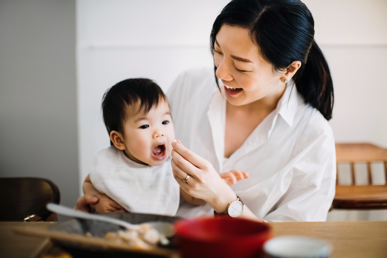 Joyful young mother feeding hungry baby girl snacks while having meal
