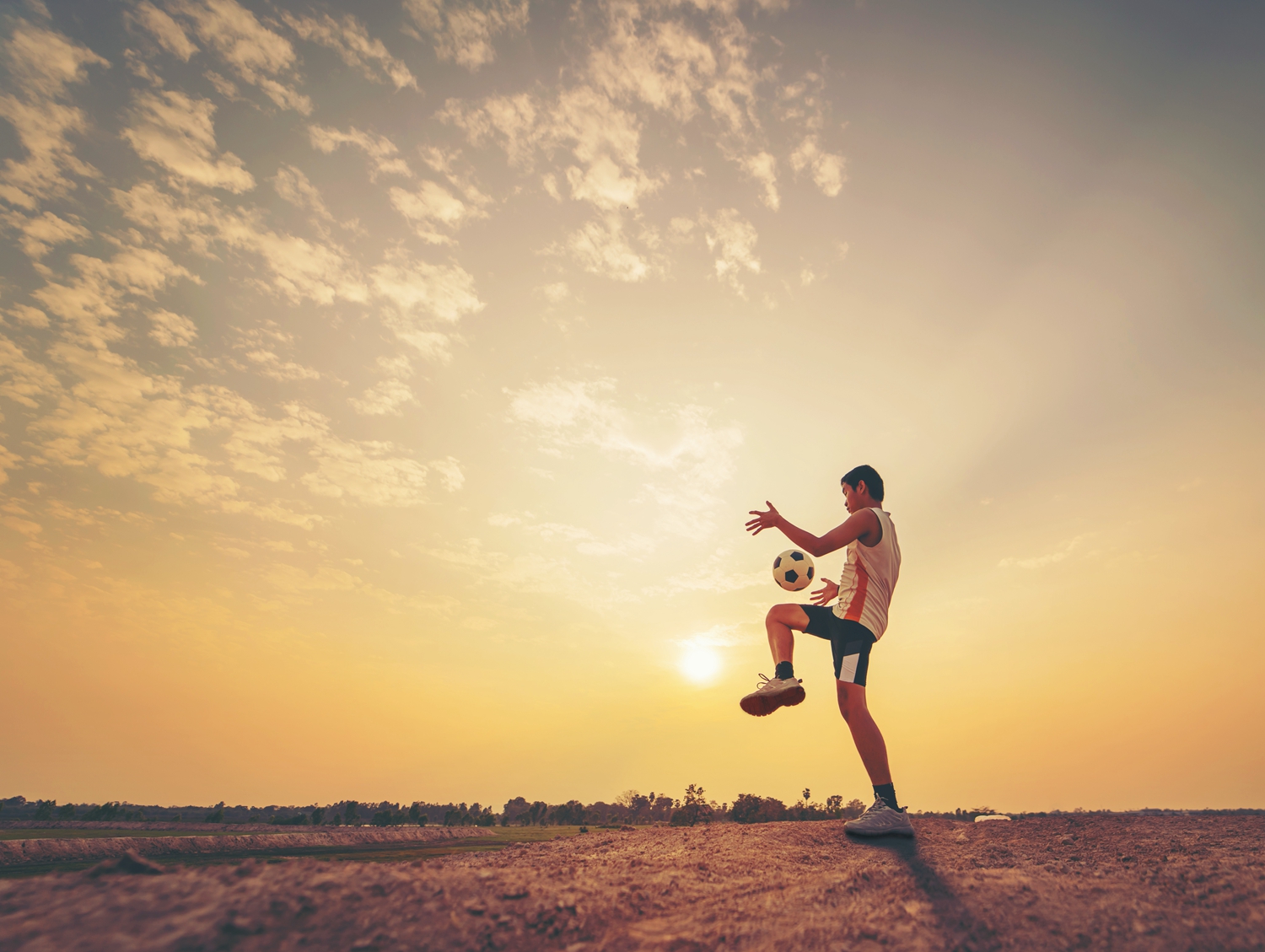 Teenager Playing Soccer On Field Against Sky During Sunset